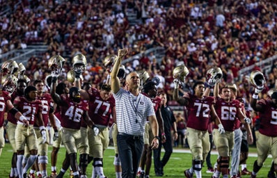 Image of FSU head coach, Mike Norvell, and the Florida State football team walking off the field in victory, holding their helmets in the air. Taken at Doak Campbell stadium.
