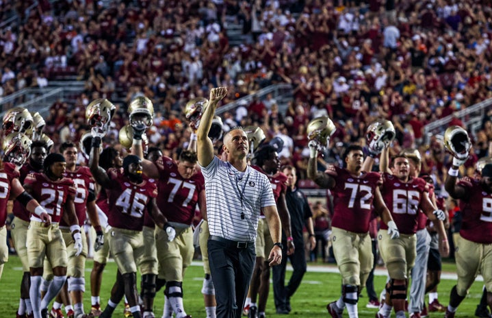 Image of FSU head coach, Mike Norvell, and the Florida State football team walking off the field in victory, holding their helmets in the air. Taken at Doak Campbell stadium.