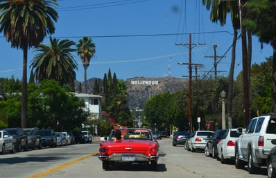 driving in red convertible with Hollywood sign in the distance