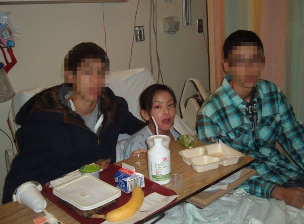 Darya sitting in hospital bed with two brothers on either side of her, post-recovery