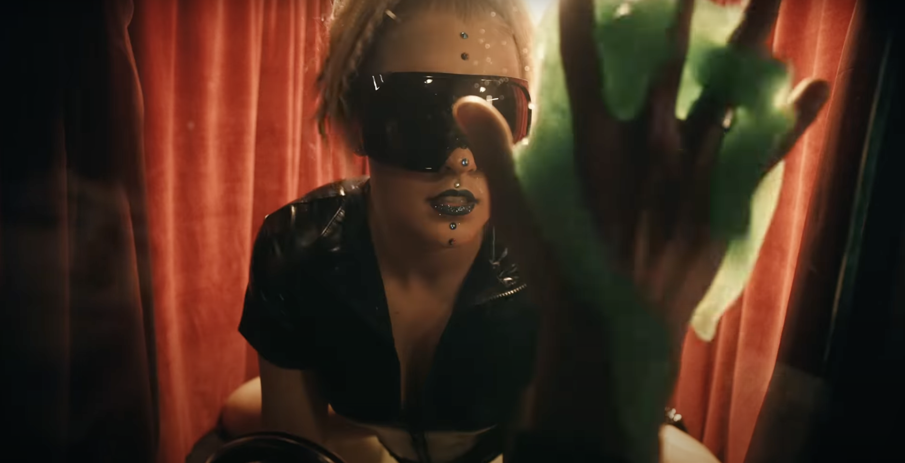 Woman (Jojo Siwa) looking from behind glass towards a hand covered in a green substance