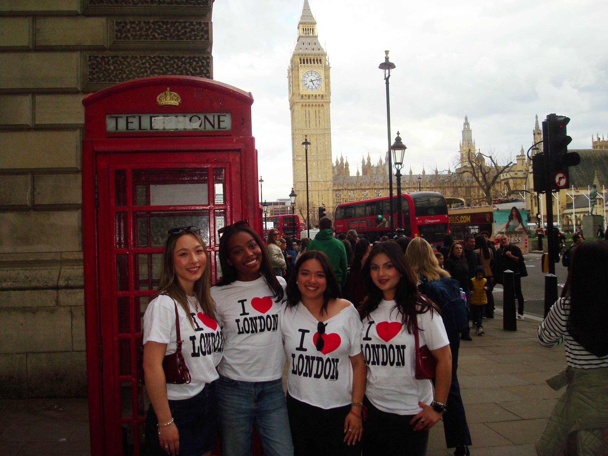four girls standing in front of Big Ben and a telephone booth, wearing \
