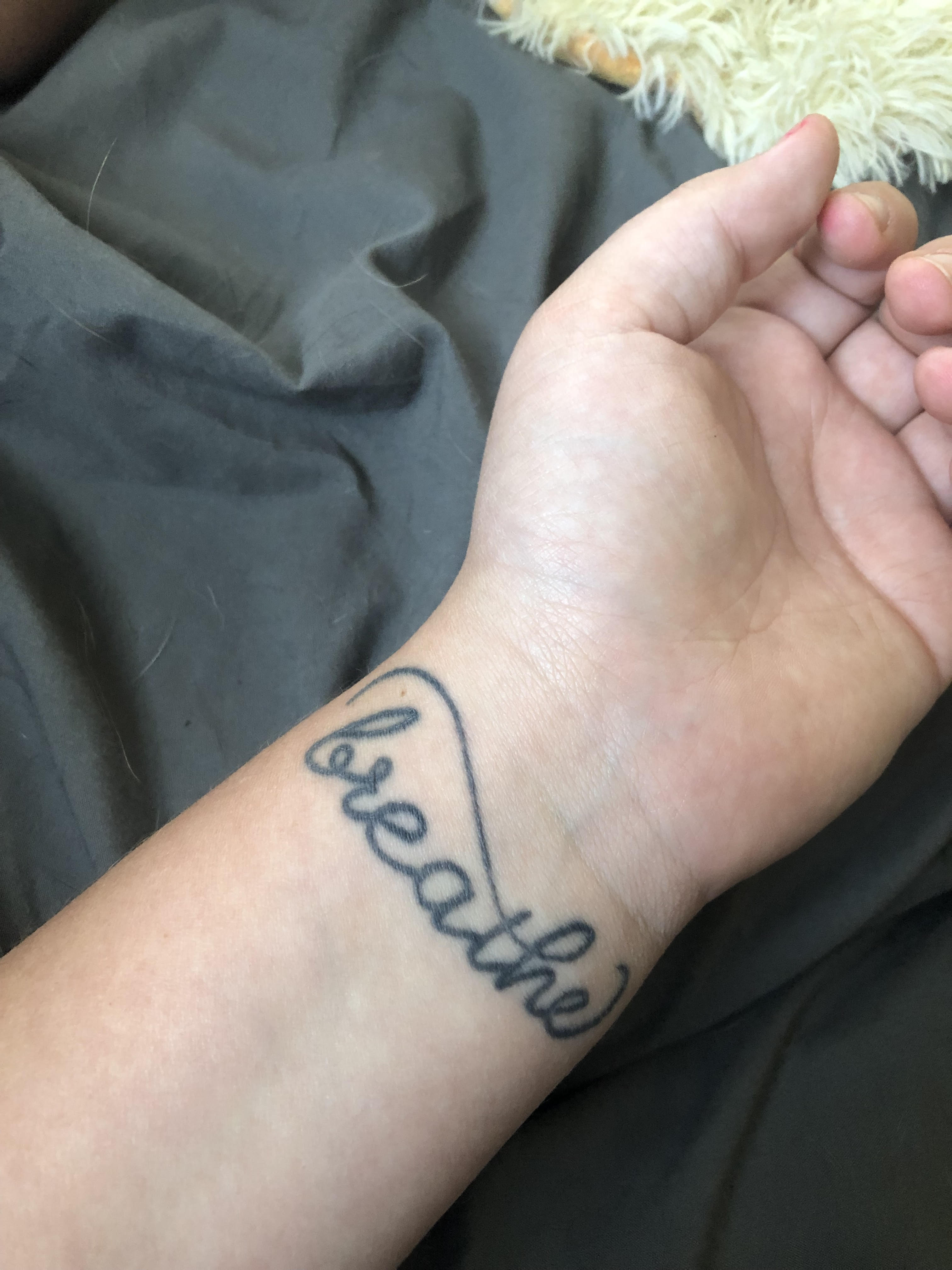 A woman\'s wrist with the cursive word \"breathe\" tattooed on it