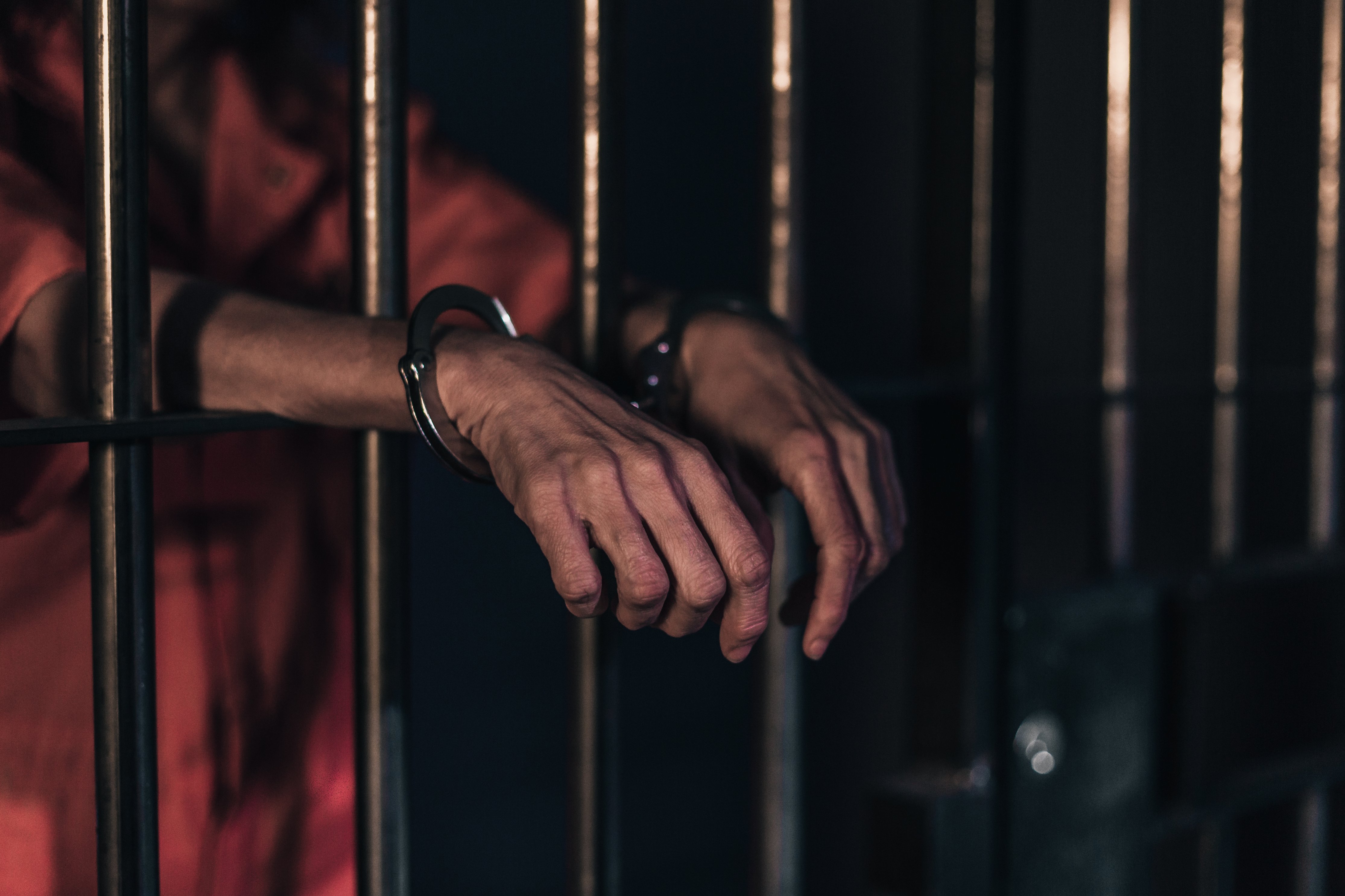 Prisoner behind bars with hands in handcuffs.