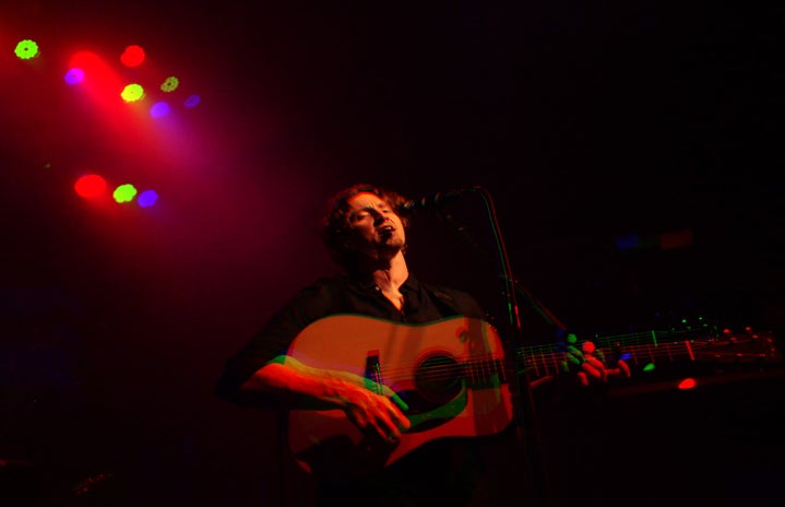 man holding guitar and singing at mic stand under various colored lights