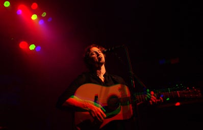 man holding guitar and singing at mic stand under various colored lights
