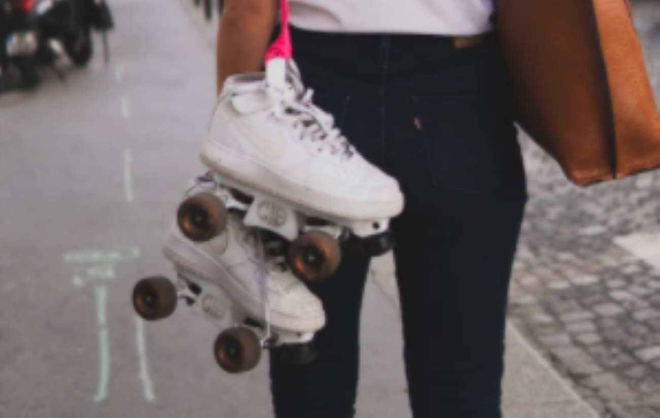 white roller skates hanging off a pink string; black jeans and brown bag.