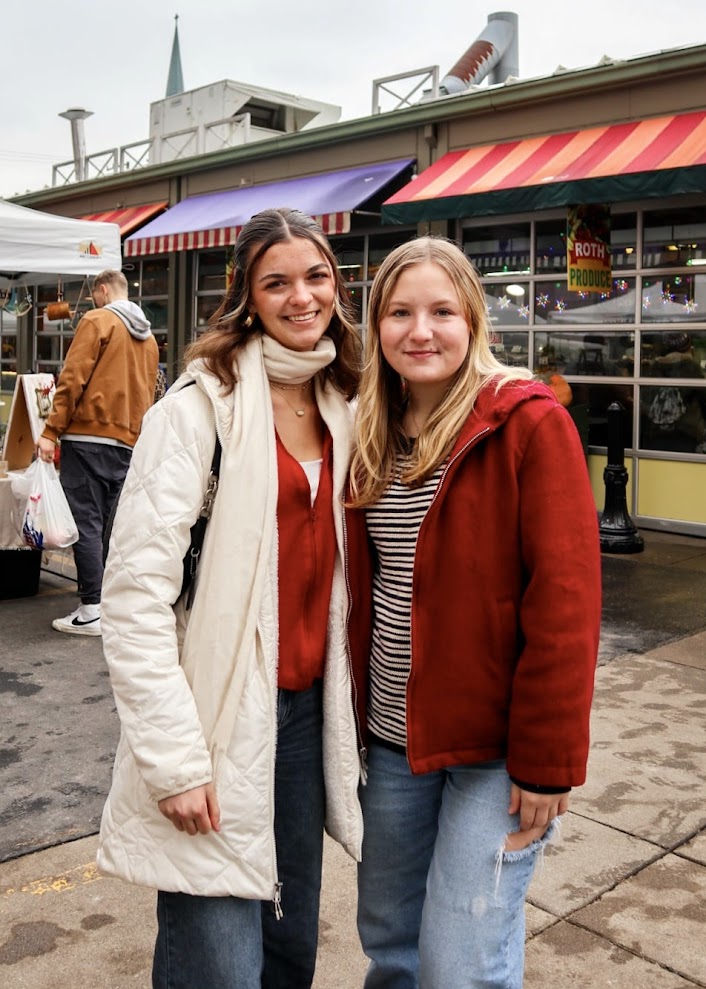 Two women pose for a photo in the winter at an outdoor holiday market.