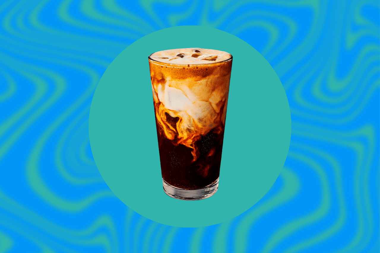 Starbucks Iced Apple Crisp Oatmilk Shaken Espresso with creamy cold foam on top, photographed against a teal and blue background
