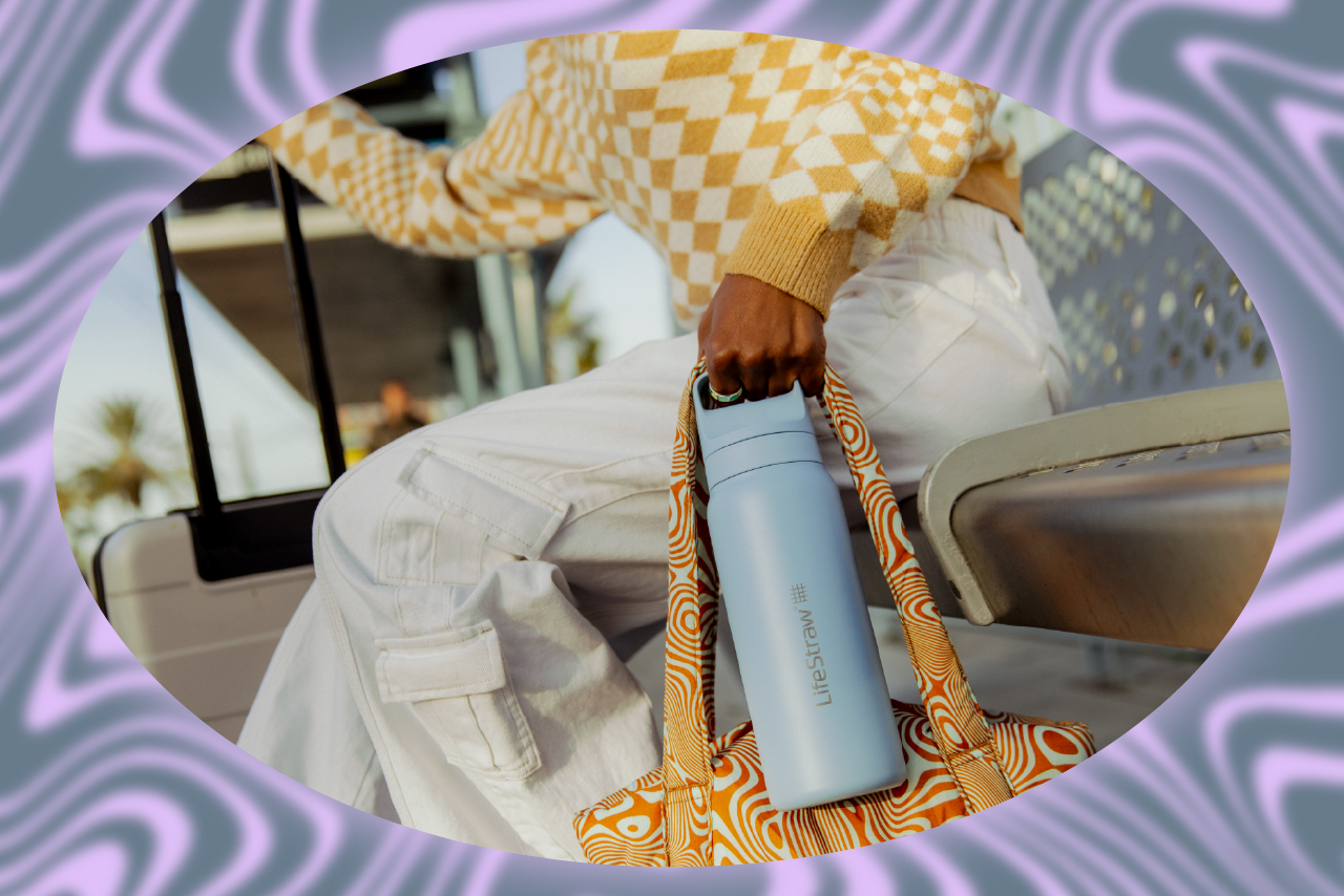 Woman in yellow checkered sweater sitting on a couch holding an orange tote bag and a blue reusable water bottole.