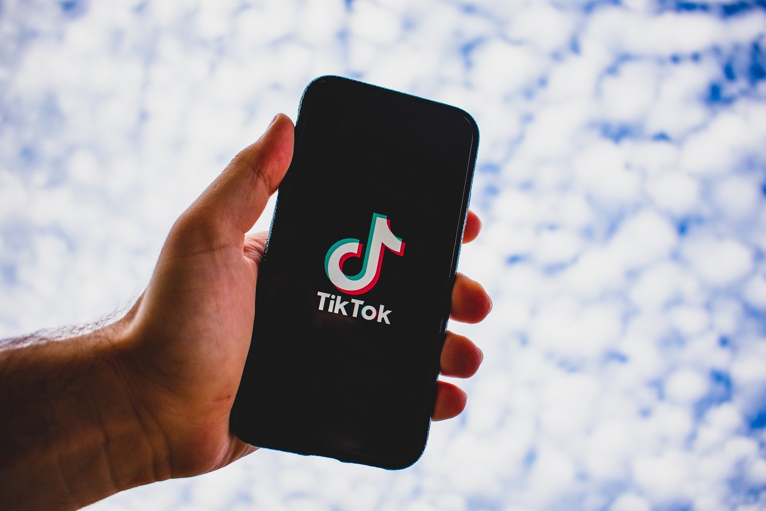 Person Holding TikTok with a Cloud Background