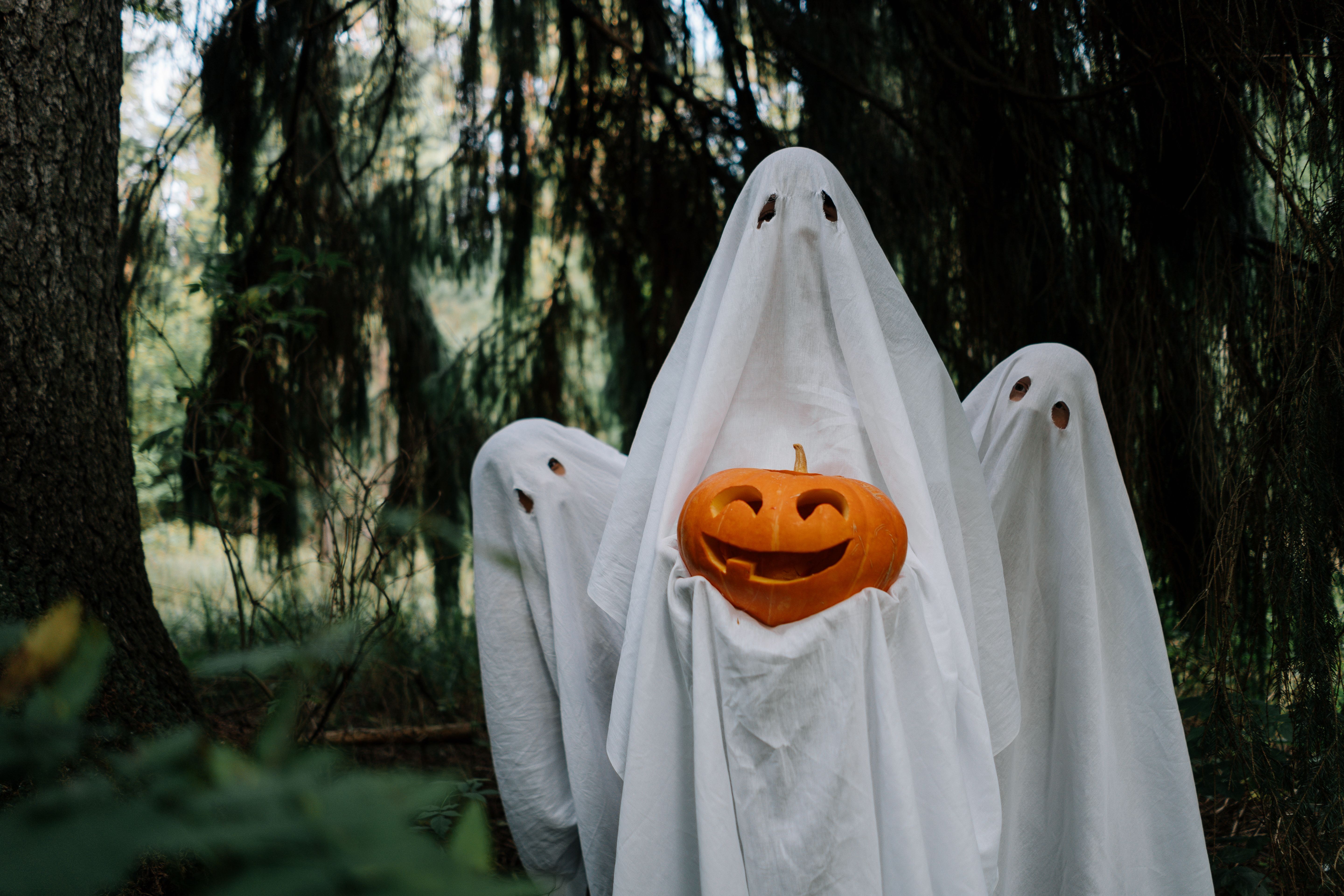 Photo of three people dressed as ghosts, one is holding a pumpkin
