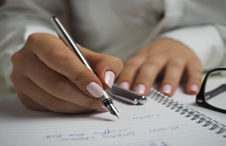 dark skinned woman with pink nail-polish writing on a notebook