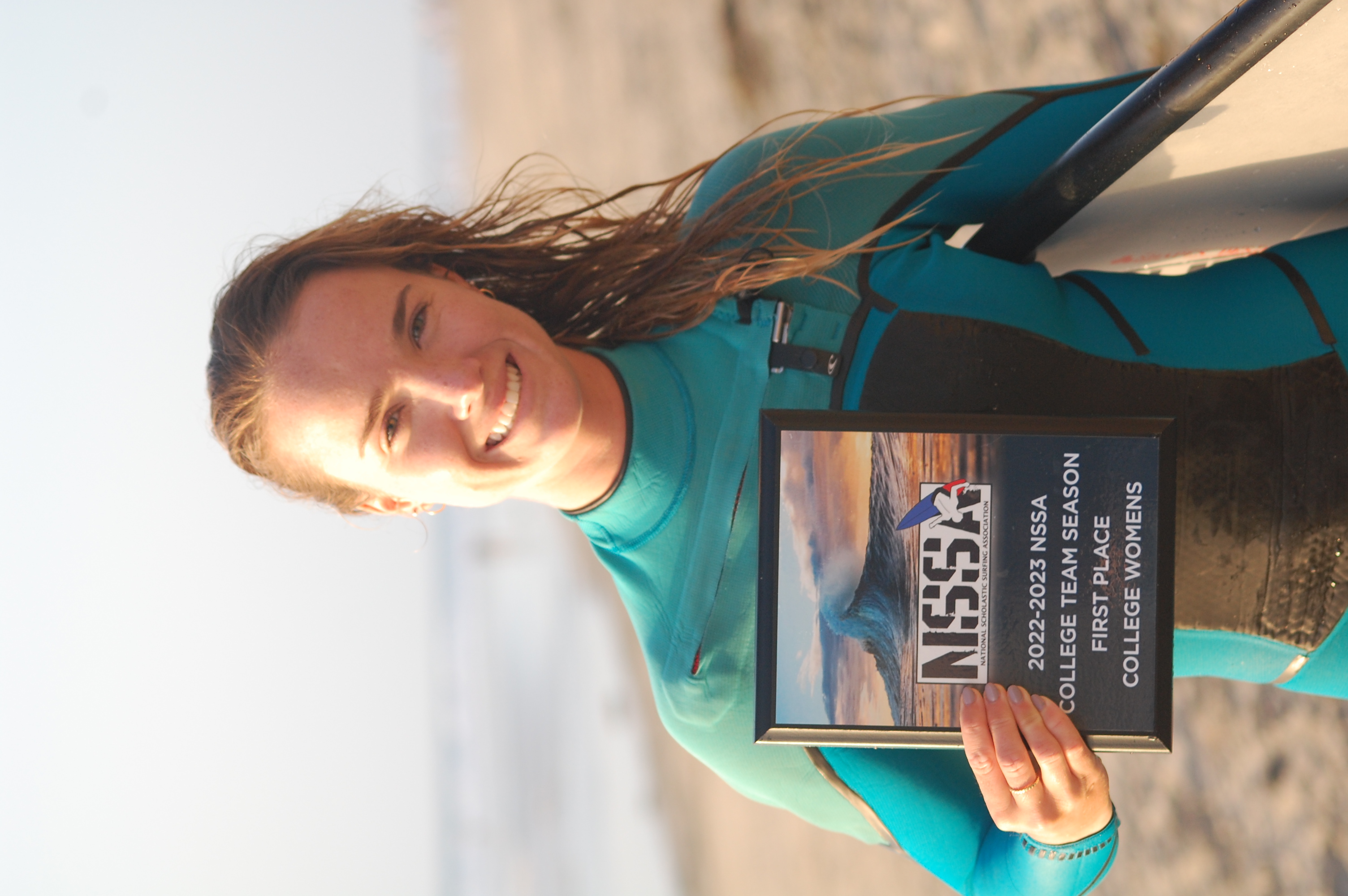 Woman at beach holding surfboard and plaque