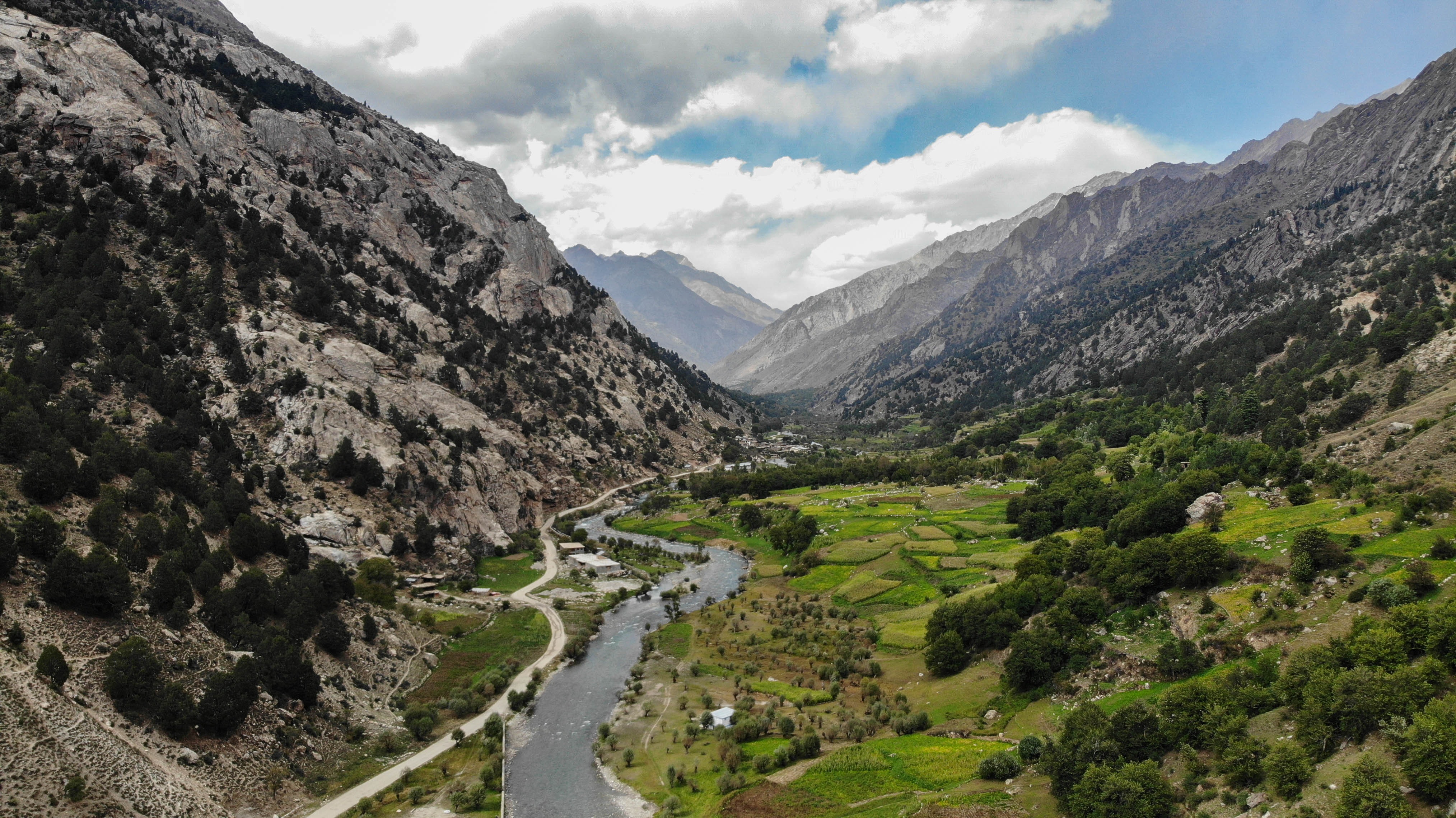 Mountains, greenery, and a river, matched by a blue sky and fluffy clous