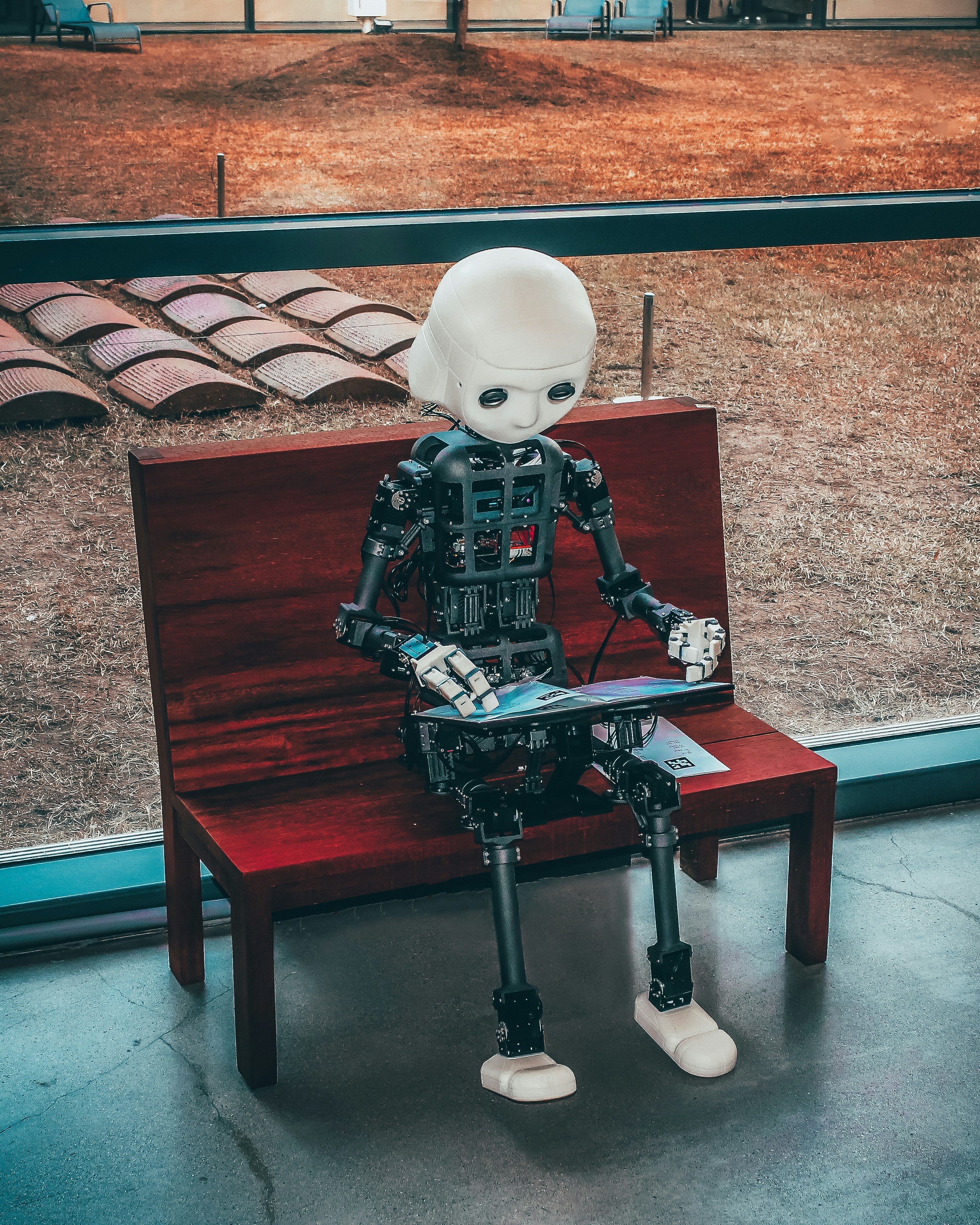 Black and white robot on red bench looking at tablet