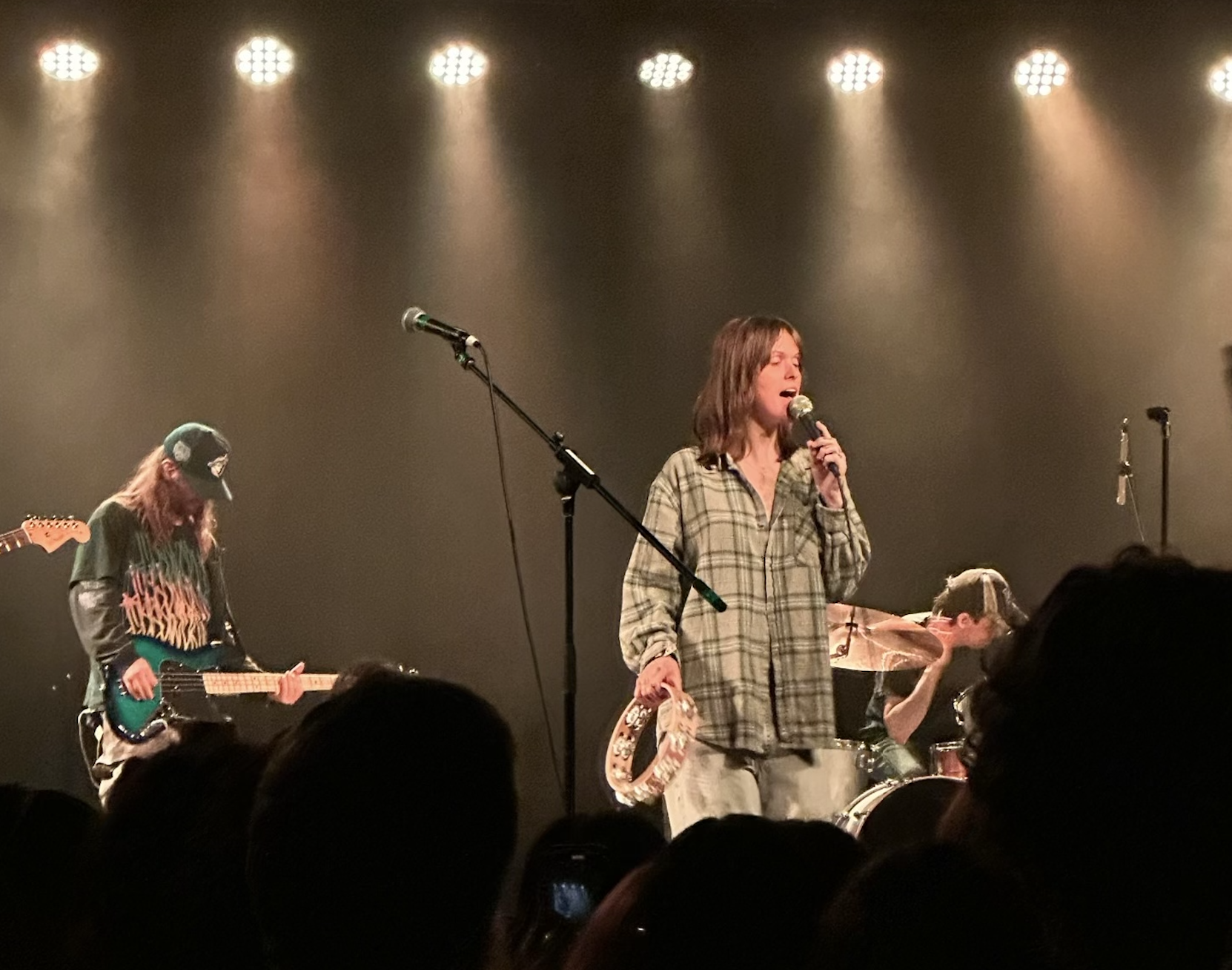 A woman stands on stage and sings into a microphone in yellow light. A man plays guitar next to her.