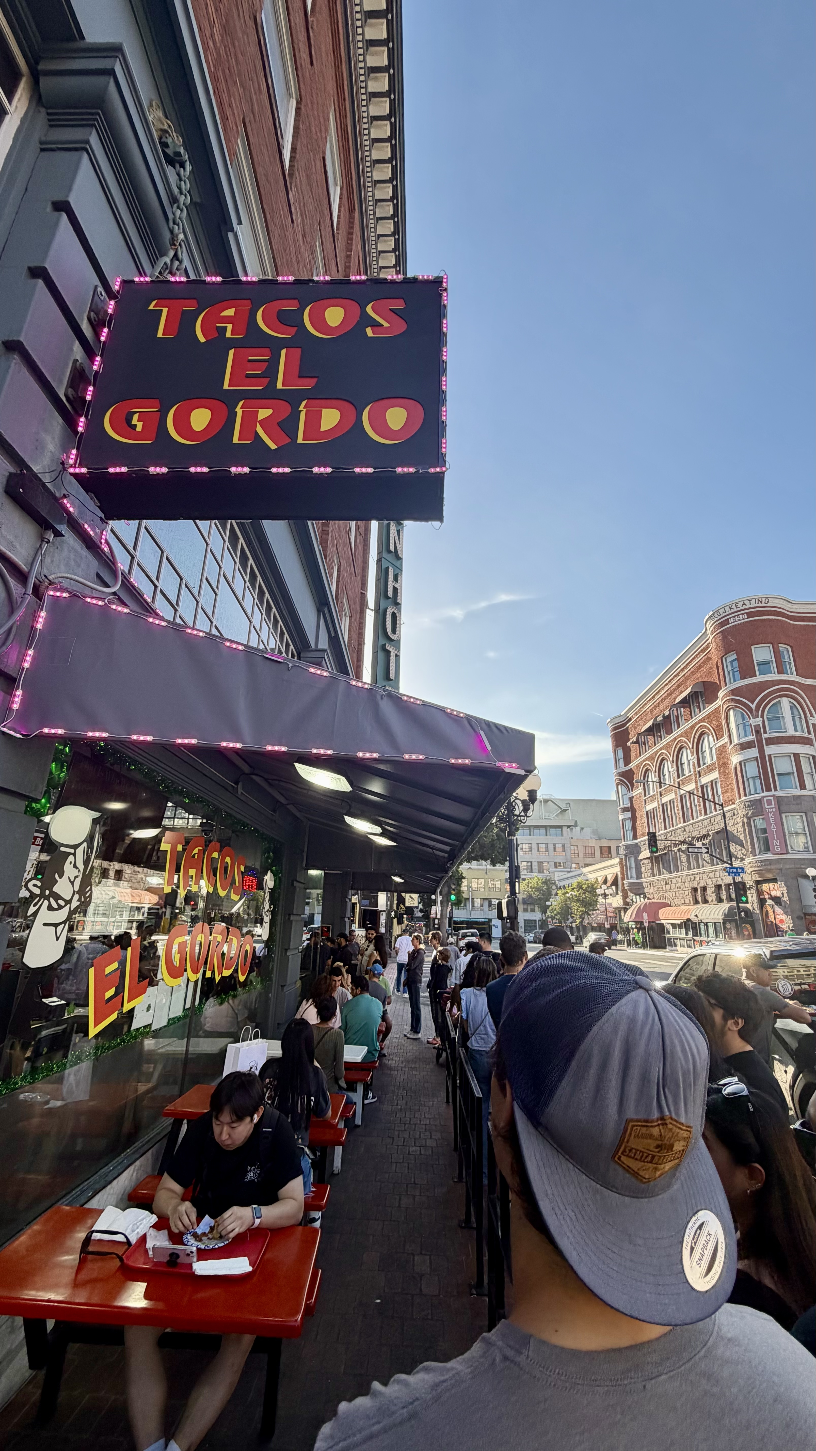 Line of customers stretching down the block outside Tacos El Gordo in downtown San Diego, with the neon-lit sign visible above the entrance.