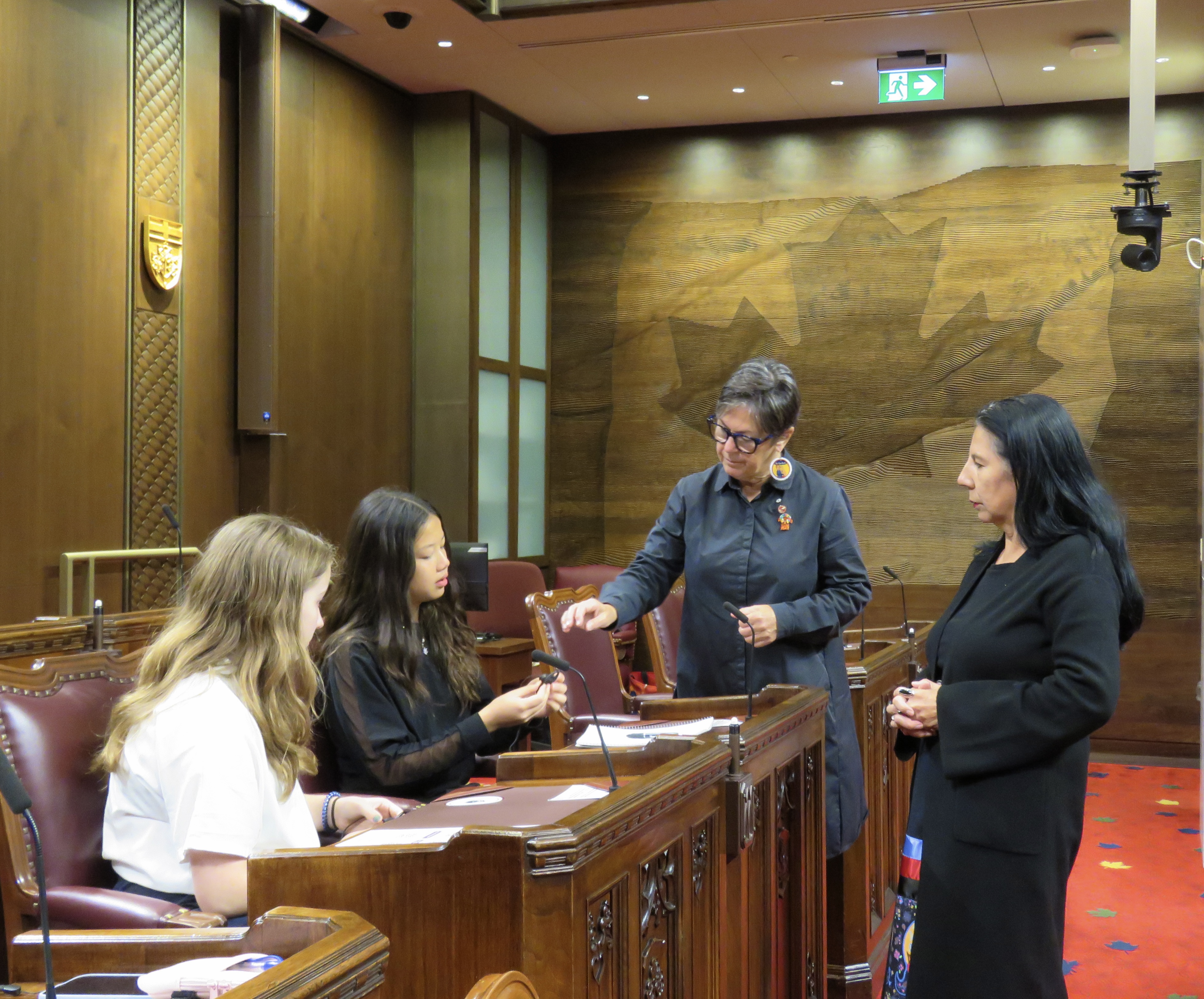 Senator Kim Pate and elder Shirley Tolley helping a pair of teen girls with their translator listening device