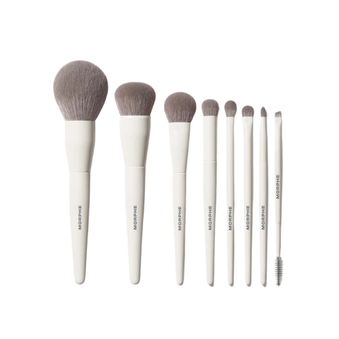 Set of eight white-handled makeup brushes of varying sizes arranged vertically. Includes fluffy, angled, and spoolie brushes, conveying a sleek, professional look.