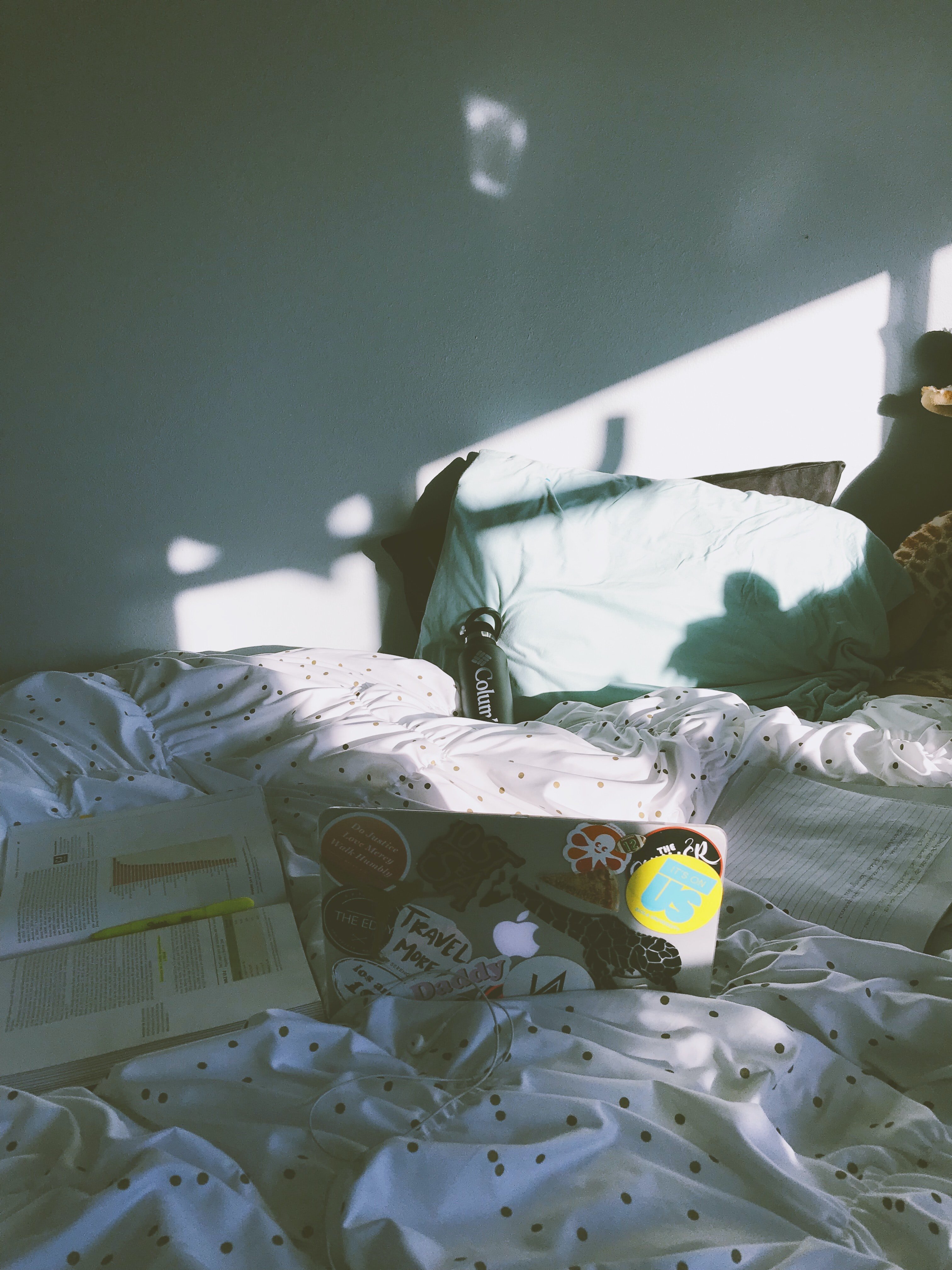 laptop with stickers and book on a bed by Kiana Bosman