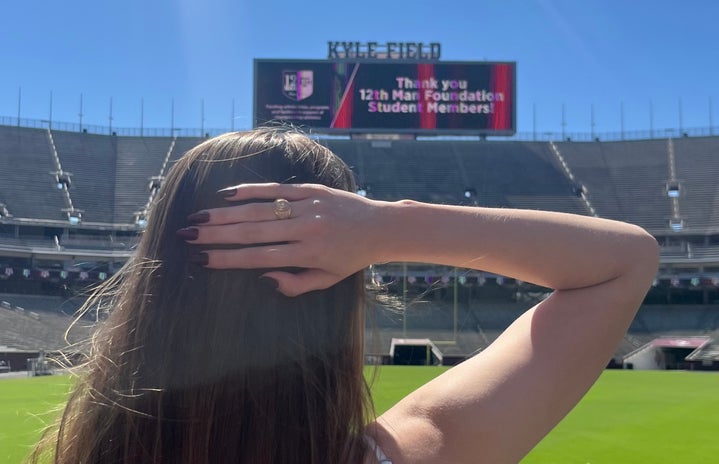 hand behind head displaying Aggie Ring inside of a stadium