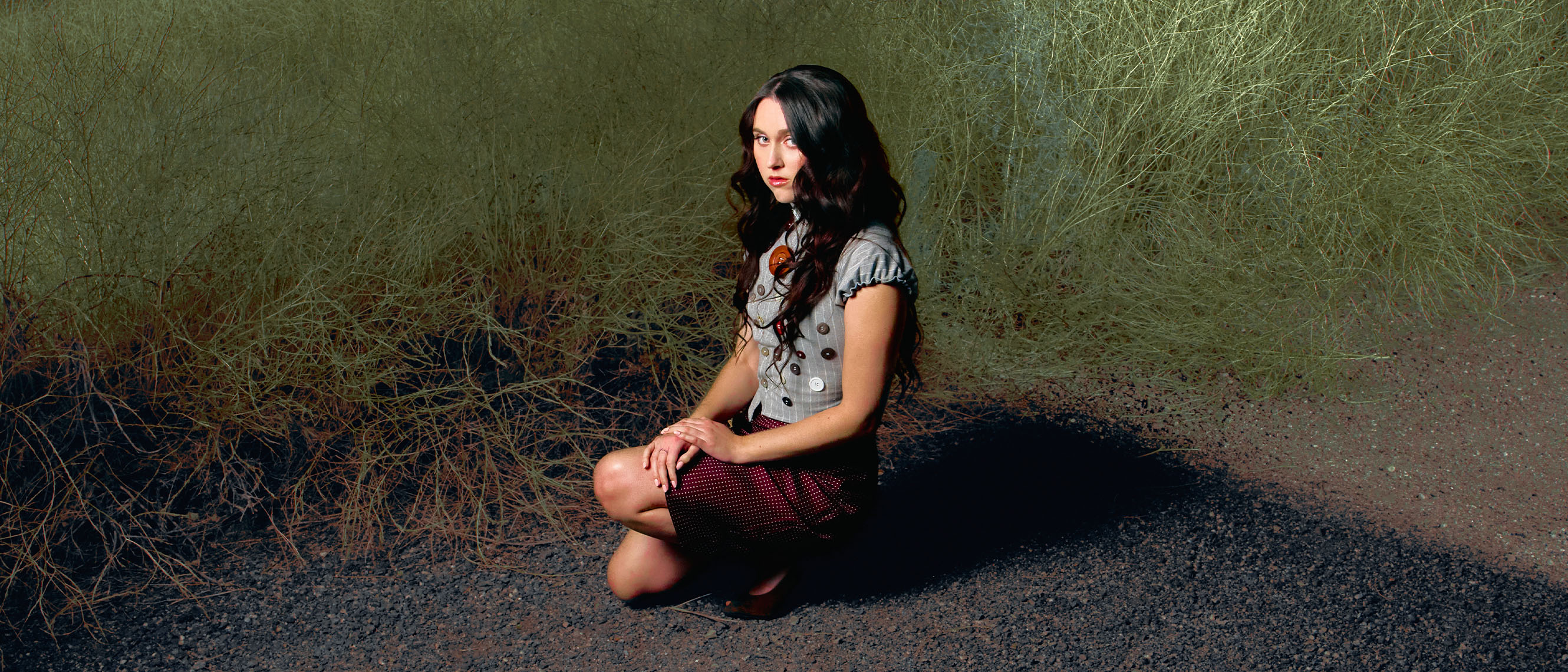 Woman, black hair, gray shirt, sitting on ground next to grass