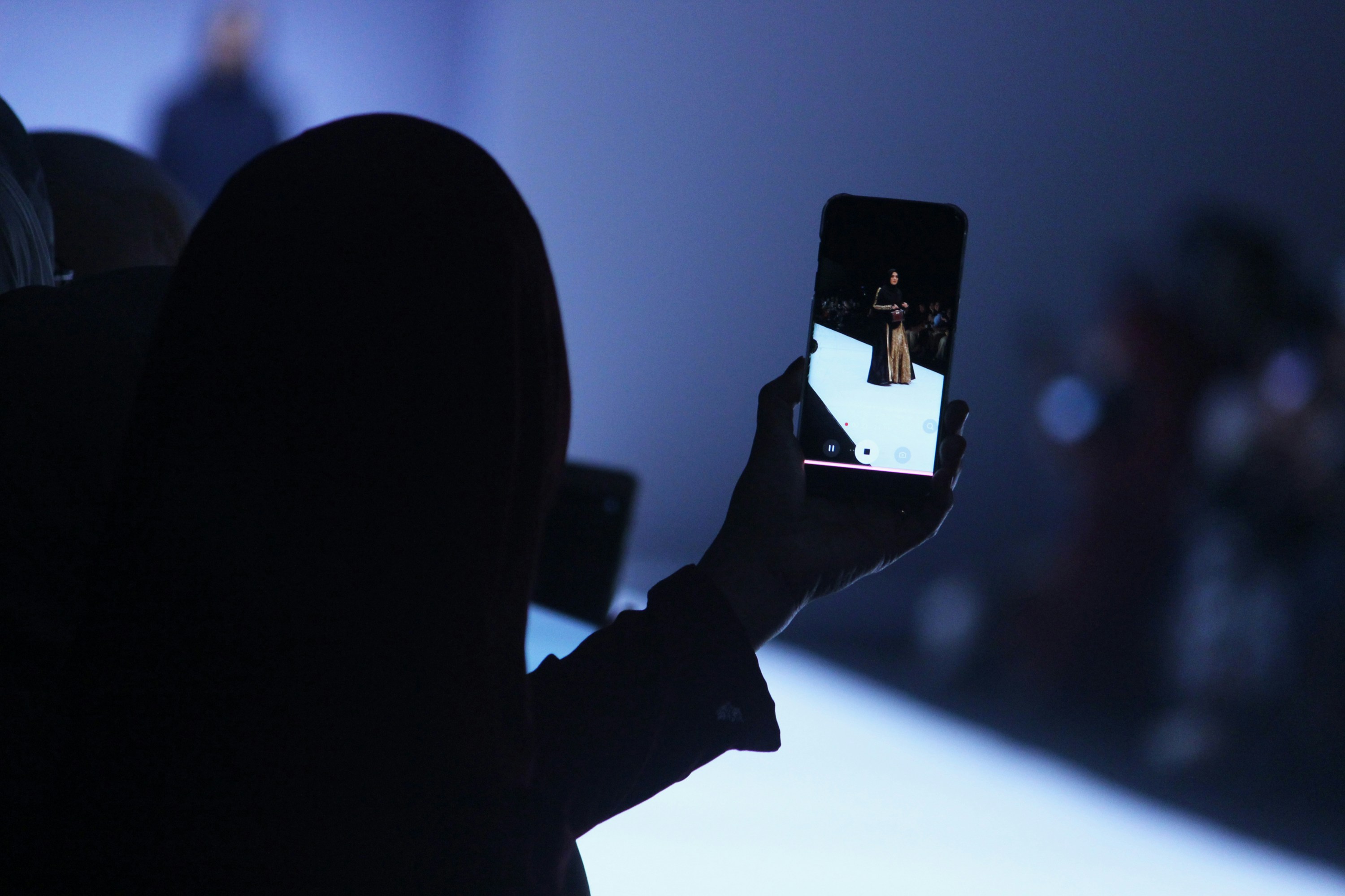 dark background with someone taking a photo on a fashion runway