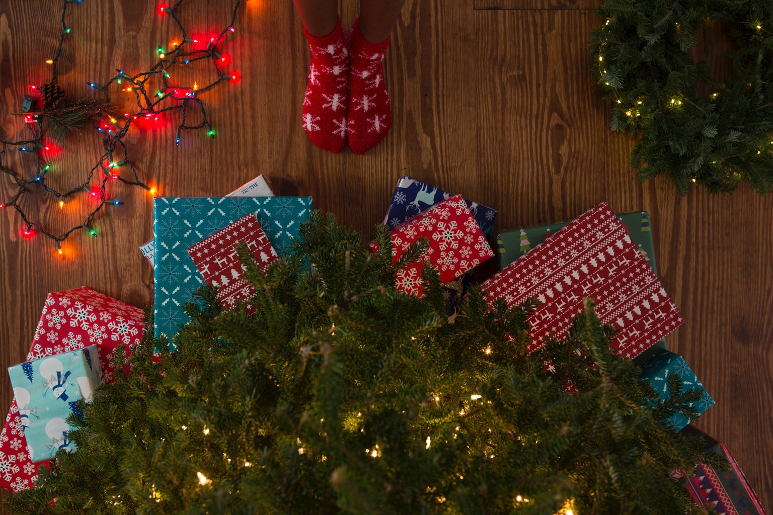 Top view of person wearing Christmas socks standing in front of Christmas tree surrounded by presents