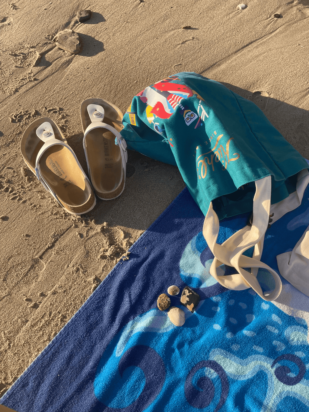 Layout of beach tote with Birkenstock sandals and collected rocks.