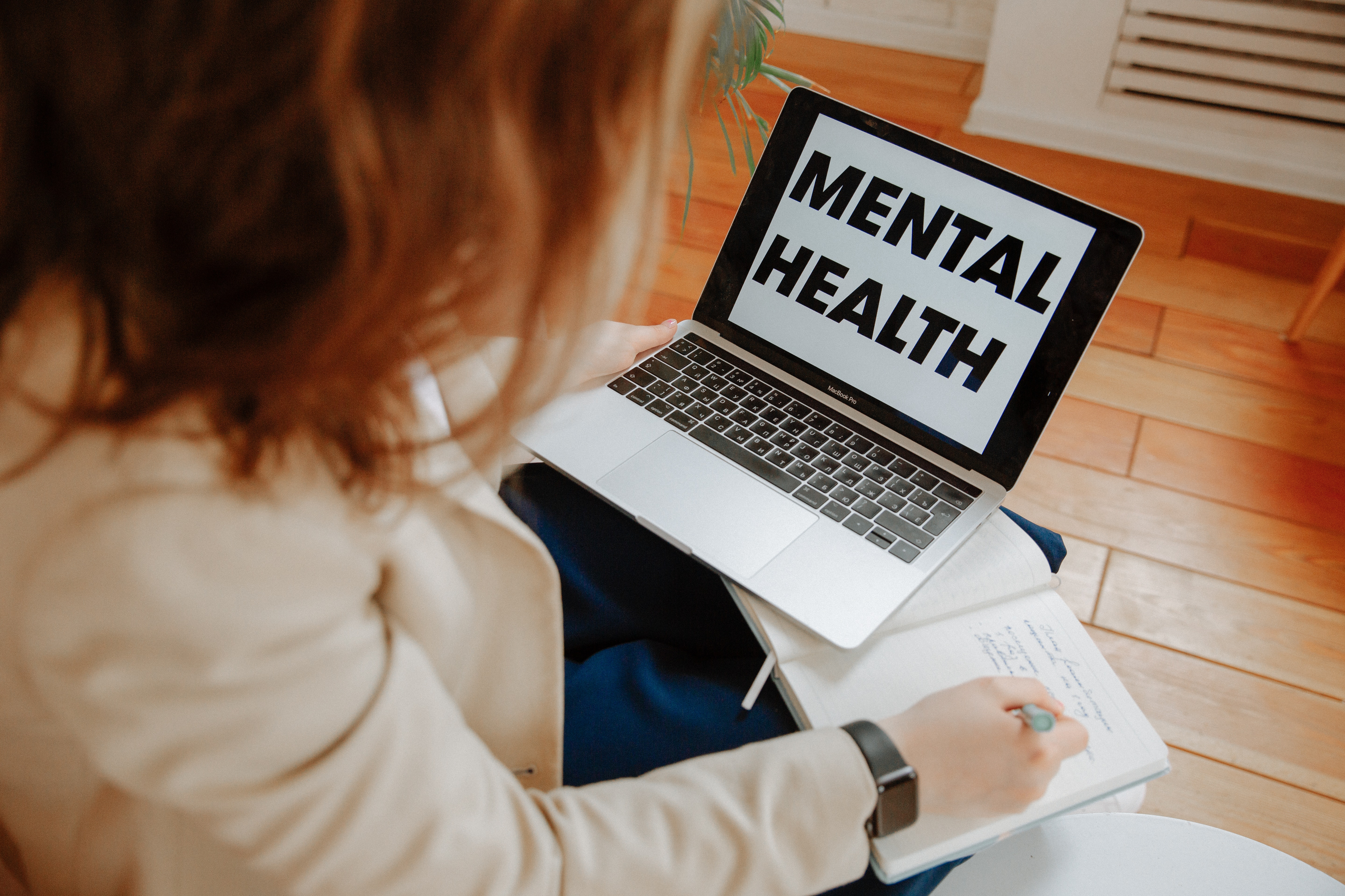 laptop open with \"mental health\" written on it while a woman writes in an open notebook