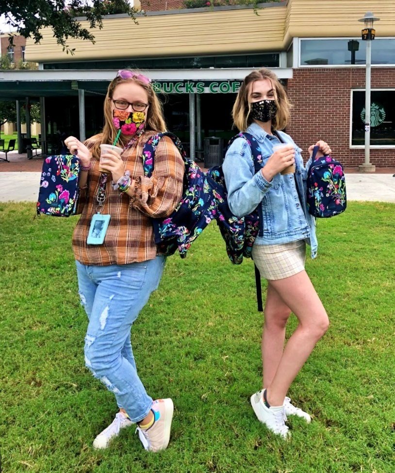 two students standing with coffee back to back