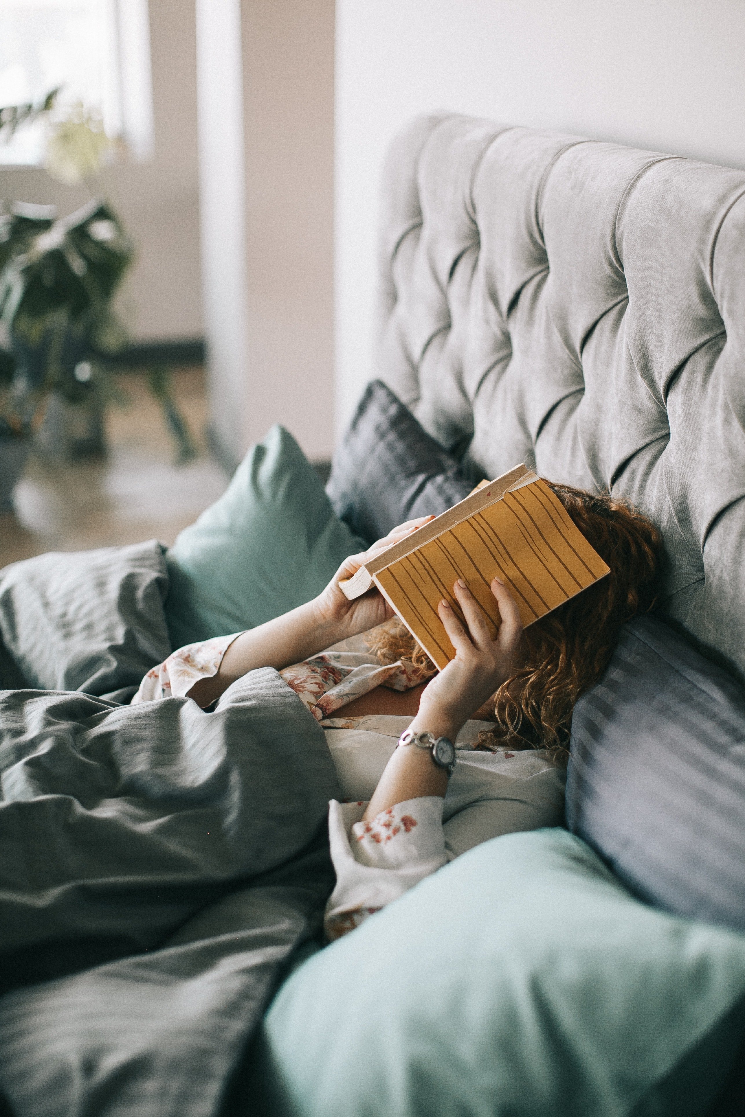 Woman Covering Face With Book On Bed