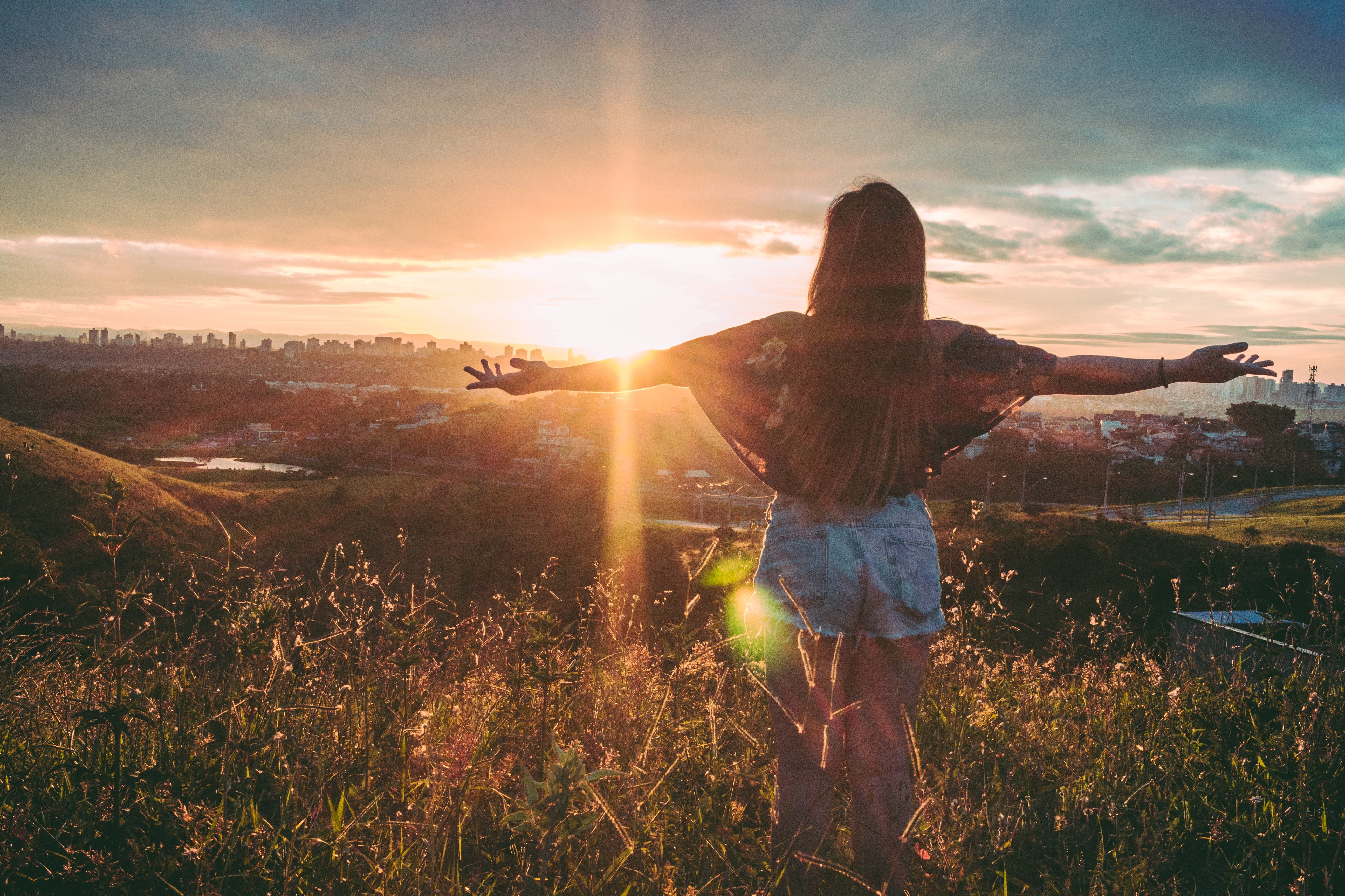 standing on mountain over field under cloudy sky at sunset