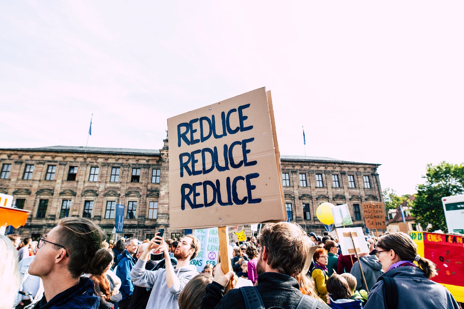 Persona holding \"reduce reduce reduce\" sign at a protest