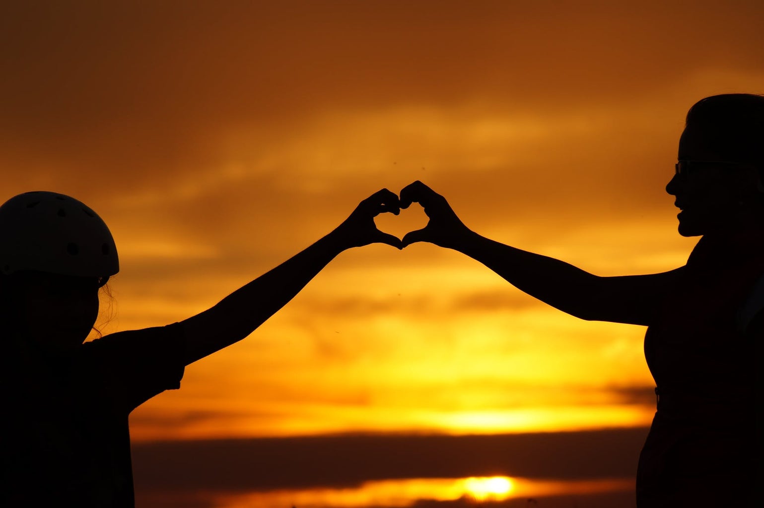 Two people holding hands in heart shape during sunset