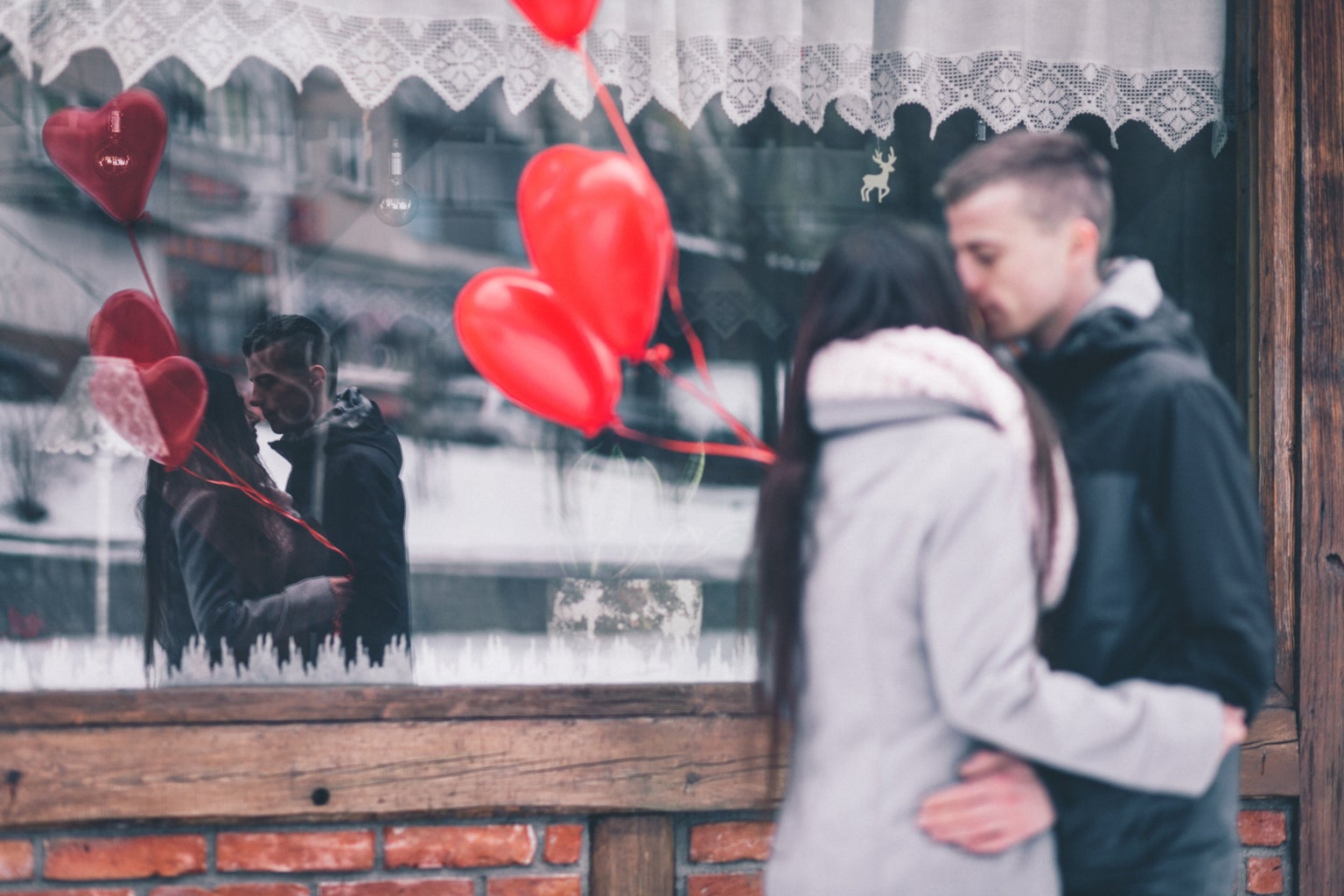 couple kissing outside a window holding red heart balloons