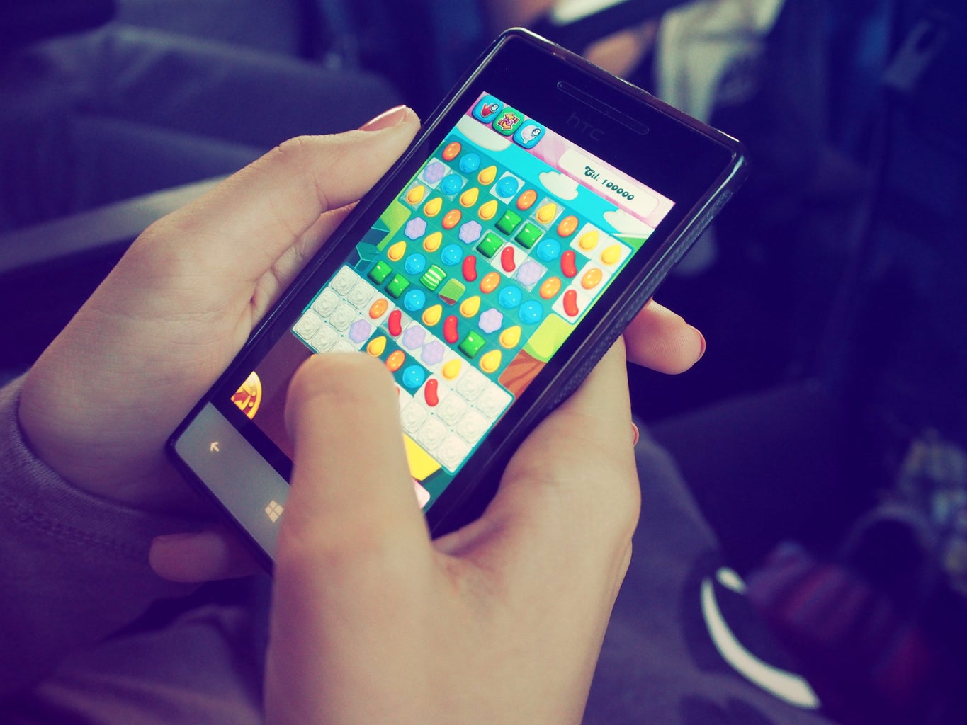 A smartphone user holds their phone, playing a game that looks like Candy Crush