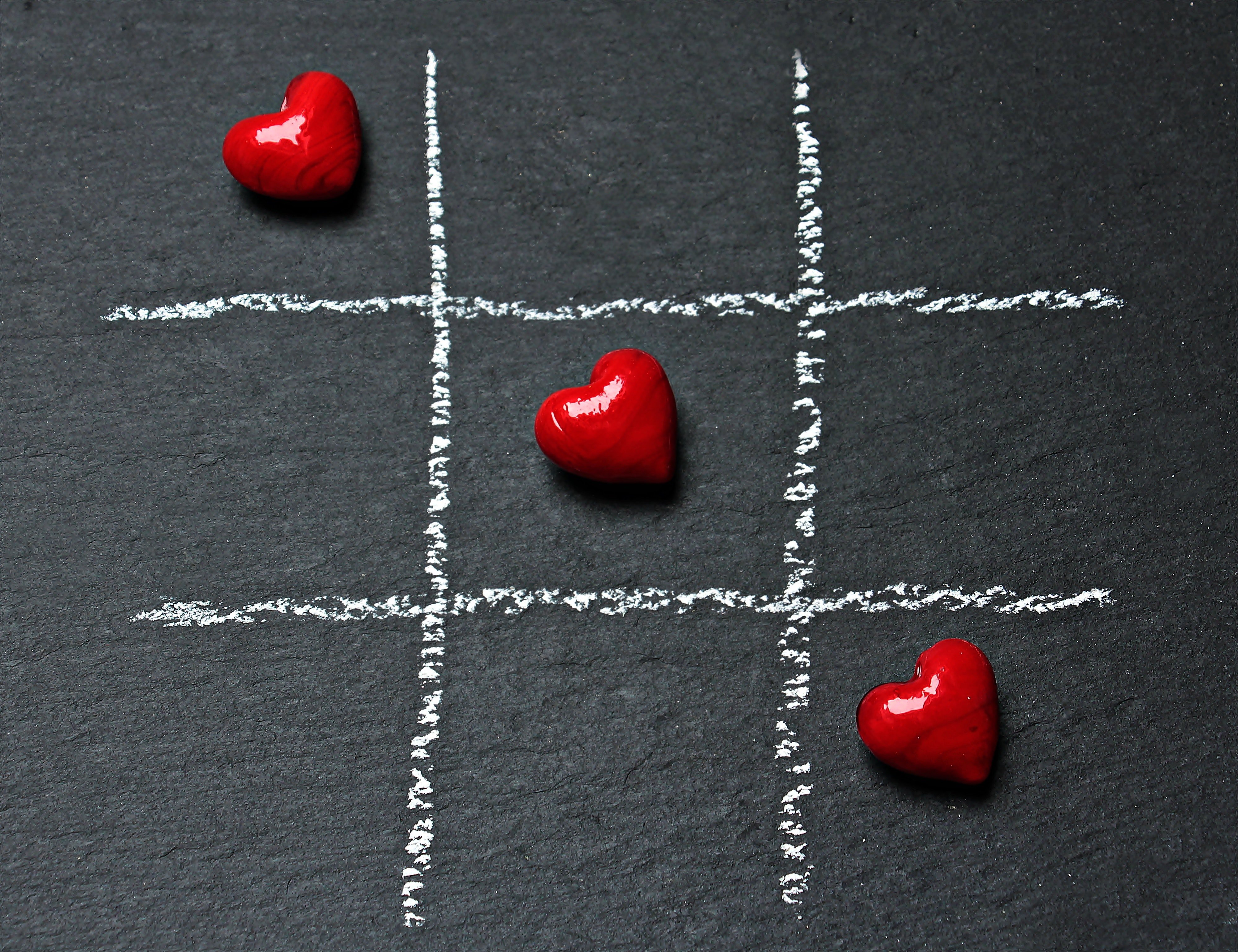 Three red candy hearts stand out against a grey background in a game of tic-tac-toe