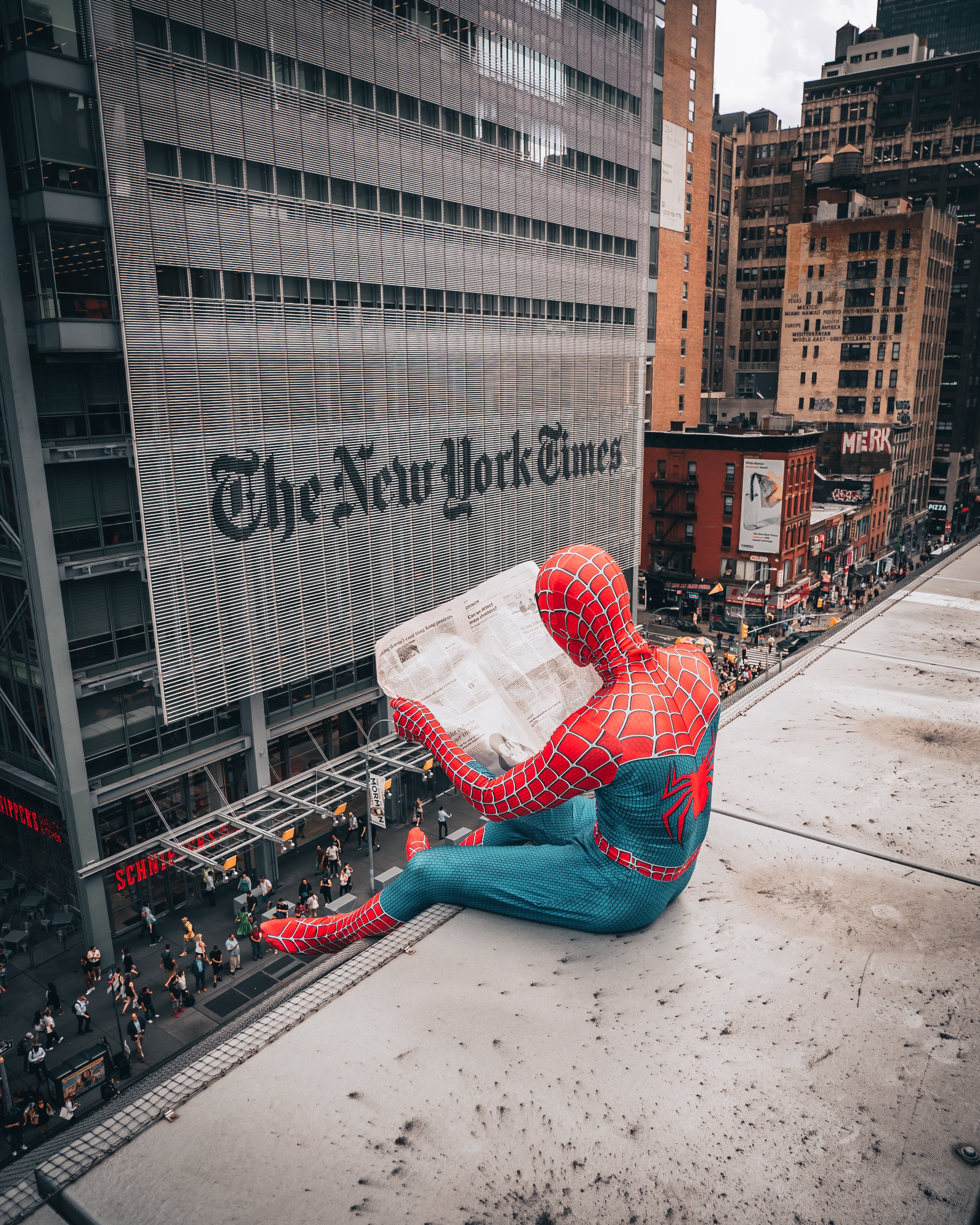 A man in a spiderman costume reads the newspaper on top of a building
