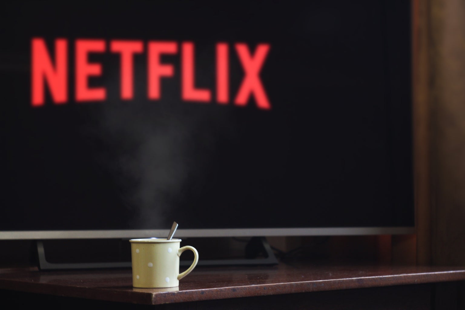 A fuzzy screen in the back ground might say \"netflix\" but the image\'s selective focus is on a mug of some sort.