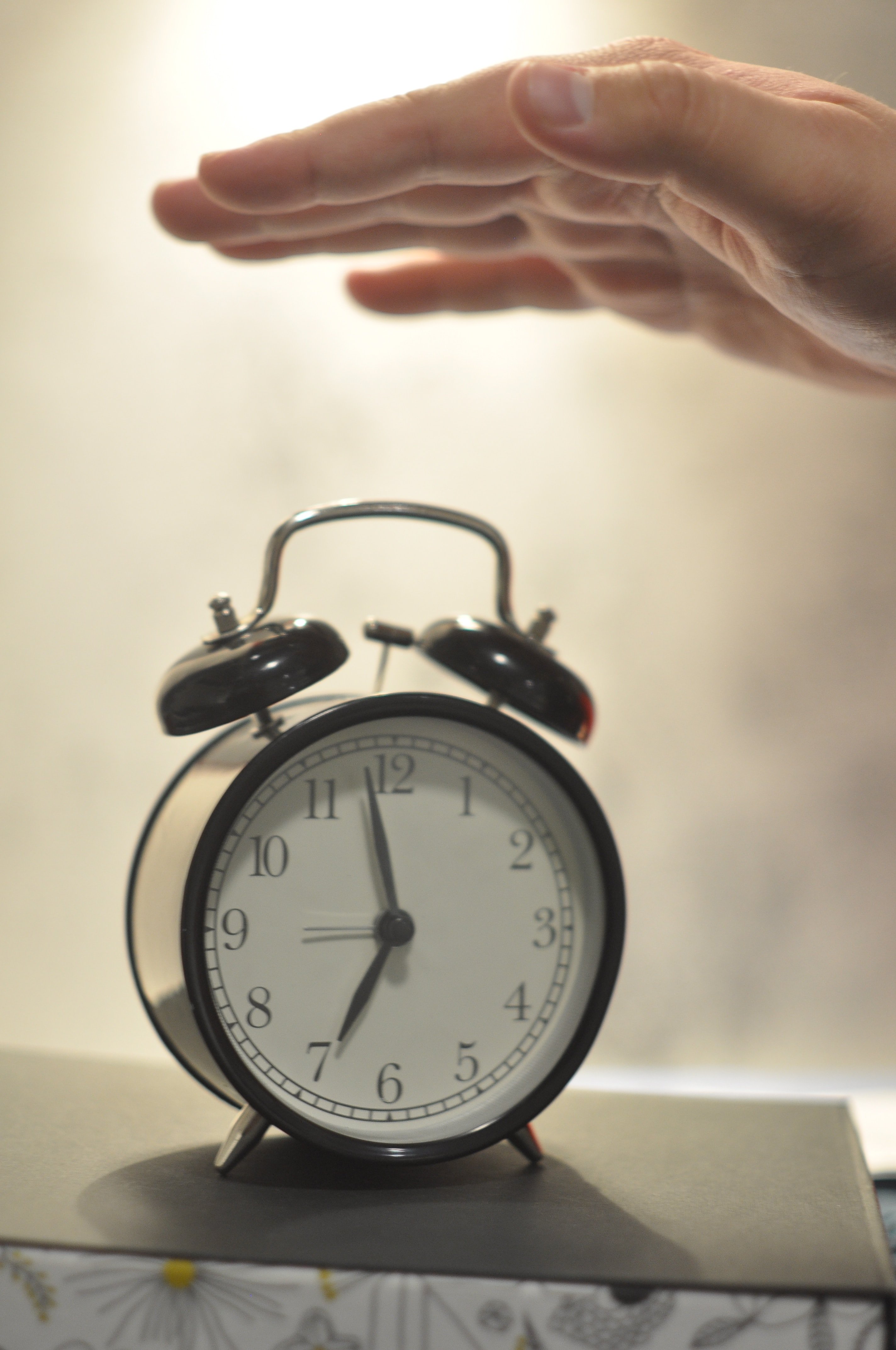 white and black alarm clock with hand on gray table