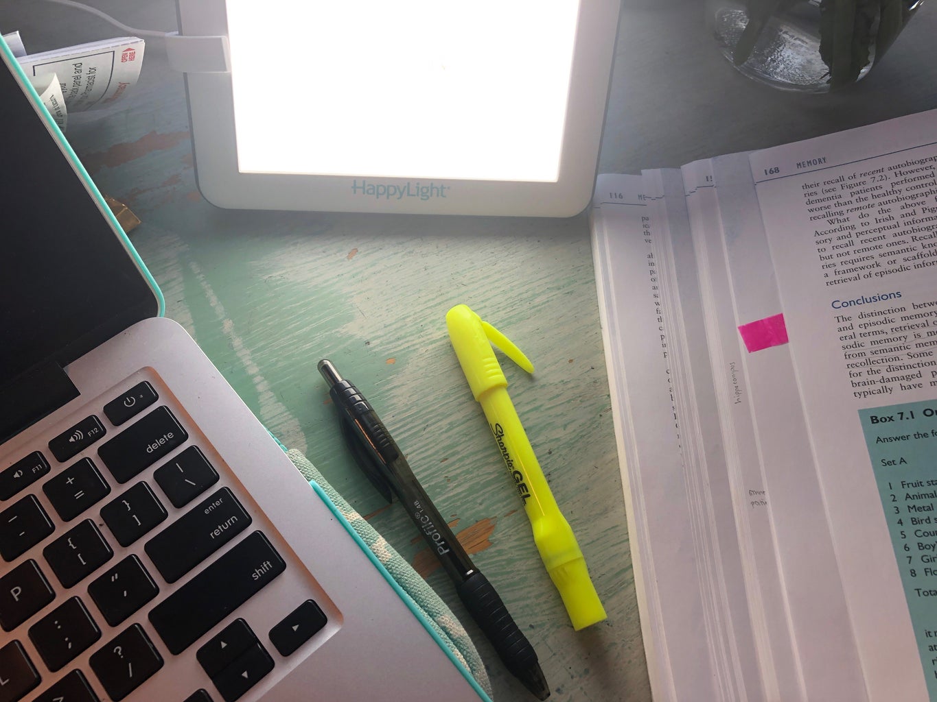 my desk with highlighters, pens, my laptop, and light therapy lamp