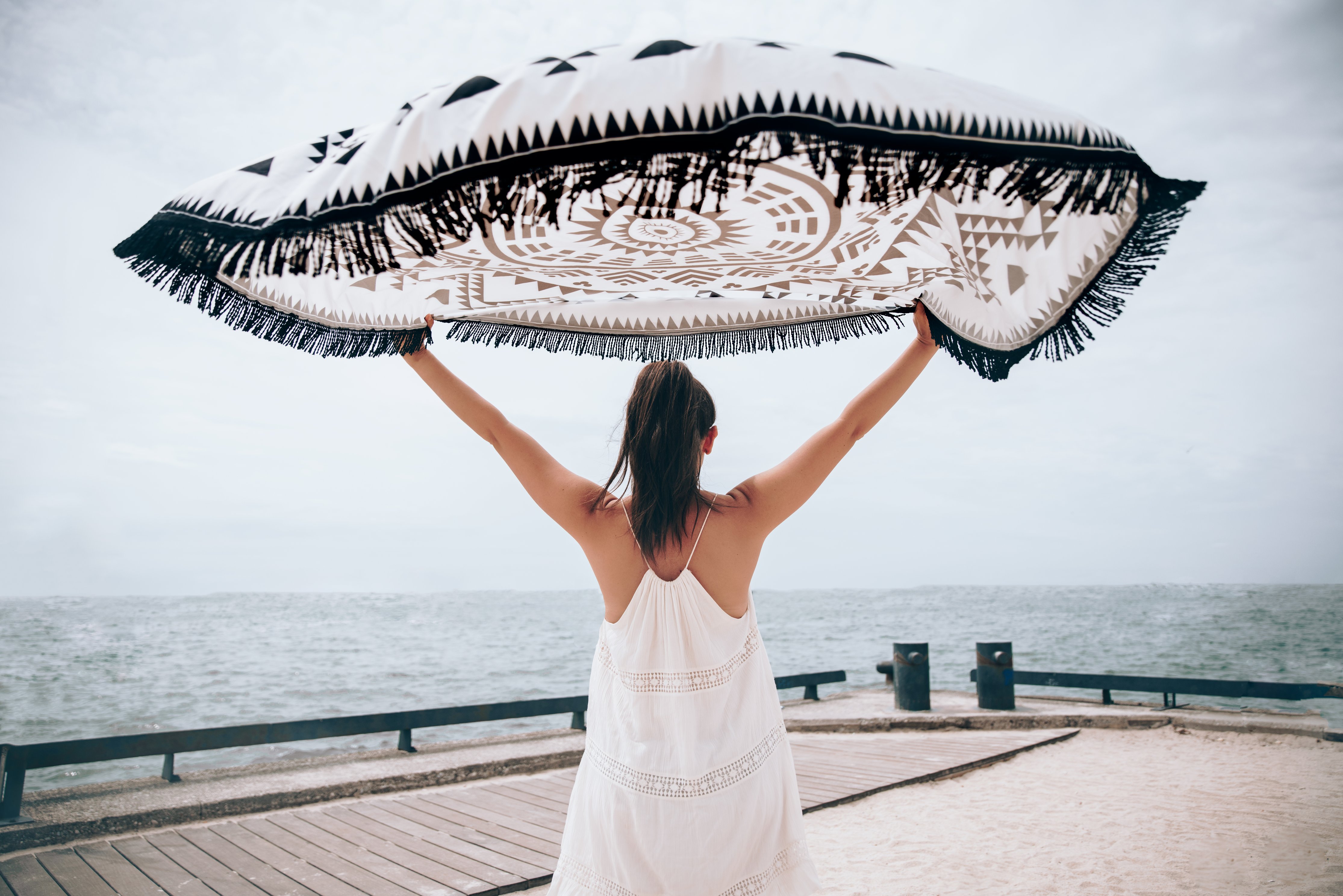 Woman at the beach holding towel above her head in the wind