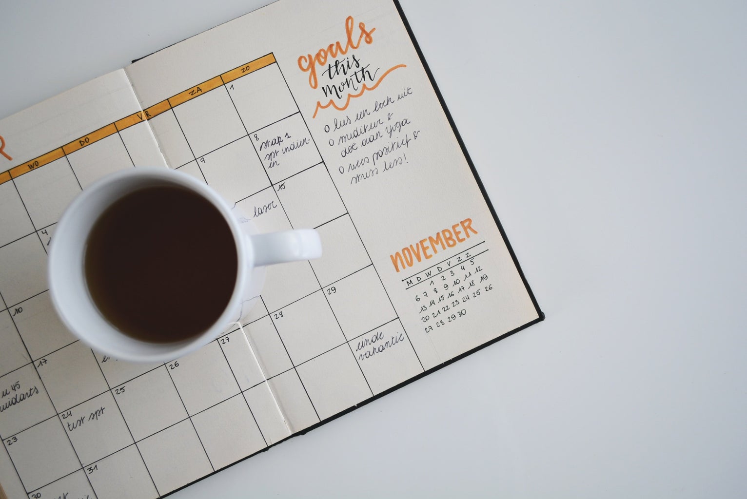 white ceramic mug with coffee on top of a bullet journal