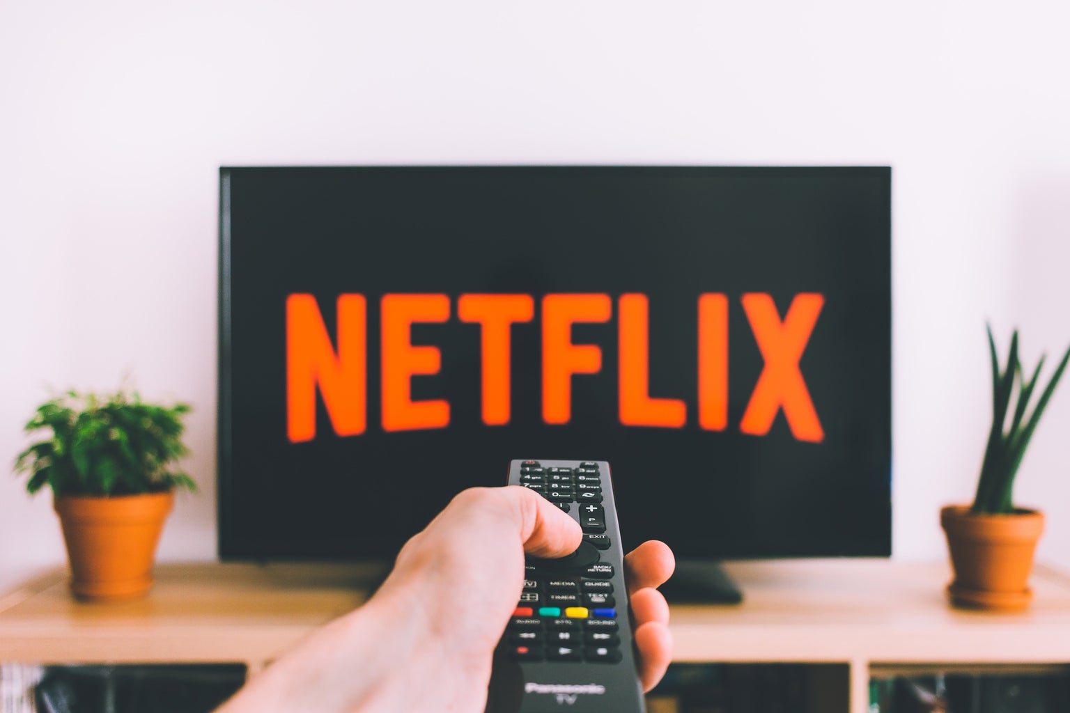 Netflix symbol on TV with a hand holding a remote