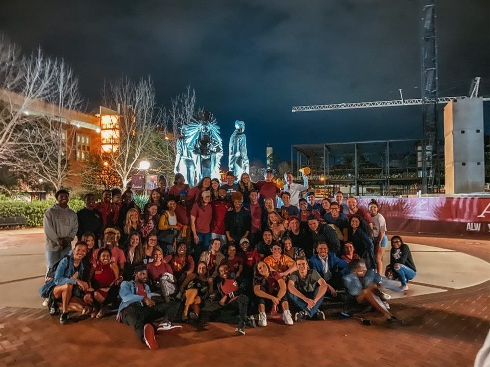 Large group of students in red shirts posing in front of a statue