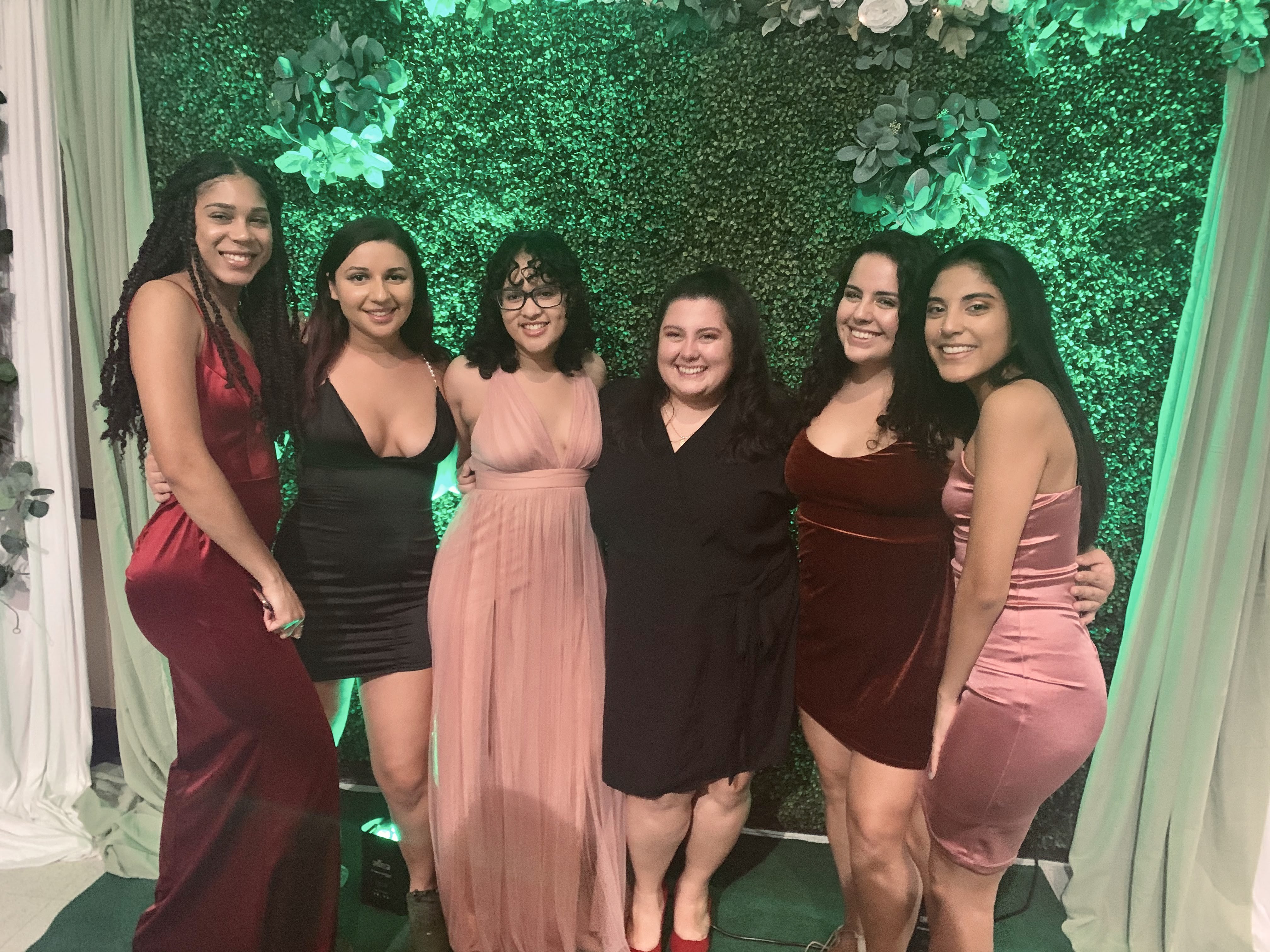 A group of women pose at a formal event in front of a green background.
