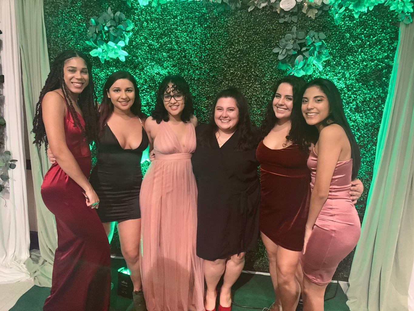 A group of women pose at a formal event in front of a green background.