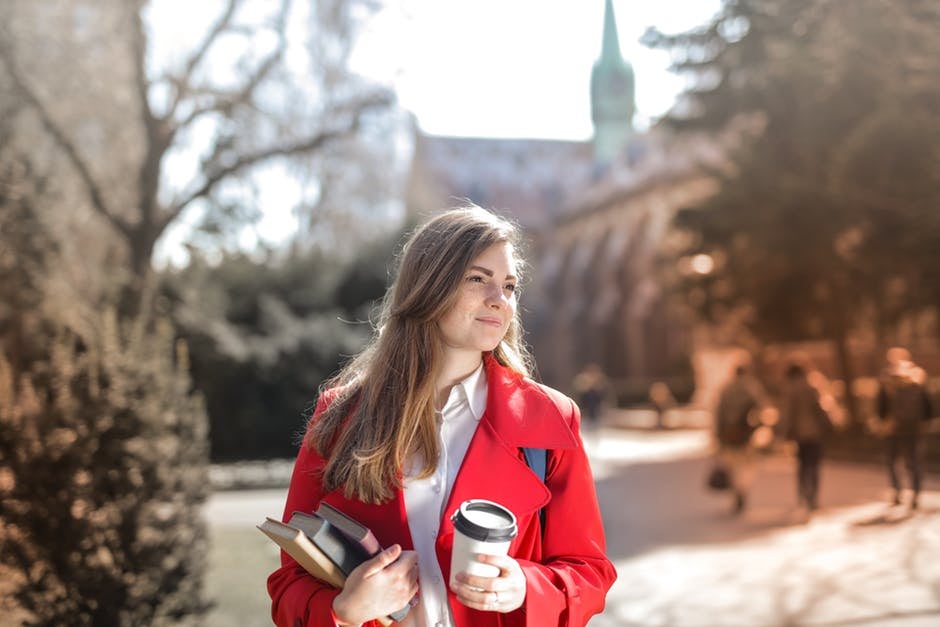 woman in red coat business casual holding books and a coffee